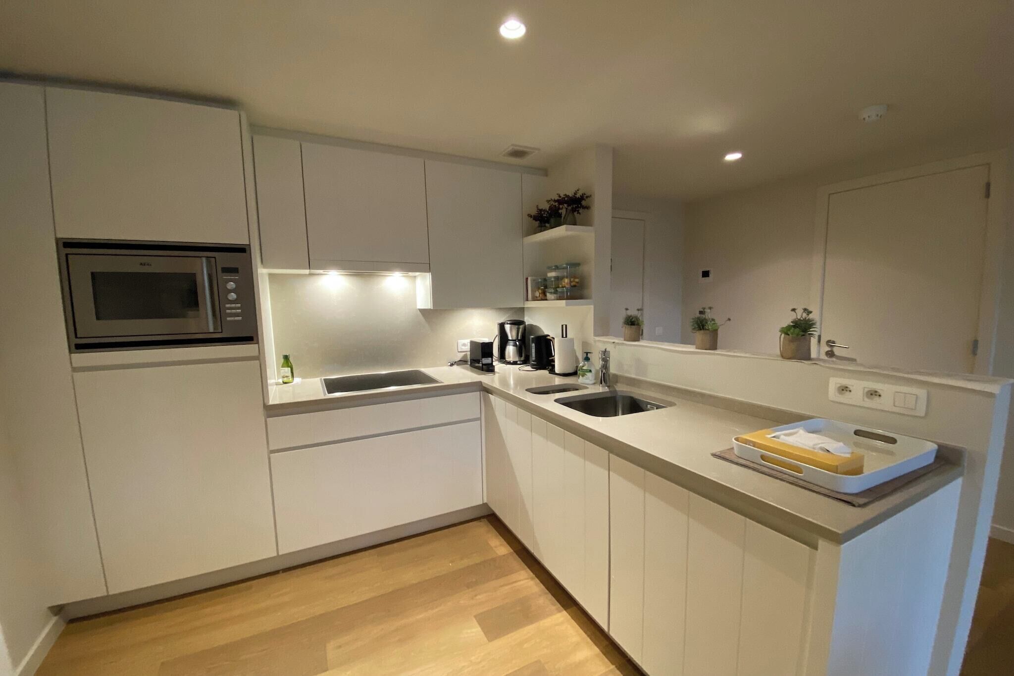 A modern kitchen with white cabinets, a built-in microwave, a sink, and a countertop with a coffee maker and a plant.
