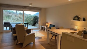 Un saló modern amb una gran finestra corredissa que dona a un balcó, una taula de dinar de fusta i seients confortables.