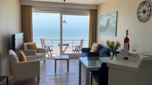 Een moderne hotelkamer met balkon, flatscreen-tv, eethoek en een schilderij.