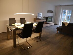 A modern living room with a dining area, a flat-screen TV, and a sofa.