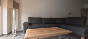 Ein modernes Wohnzimmer mit einem grauen Ecksofa, einem Holztisch und einer Stehlampe.