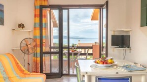 Une pièce avec un canapé, une table sur laquelle se trouvent des fruits, un ventilateur, une télévision et une vue sur la mer.