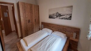 A bedroom with a wooden bed, a wooden wardrobe, and a mountain landscape painting on the wall. - Ferienwohnung in Bayrischzell (Bayrischzell)