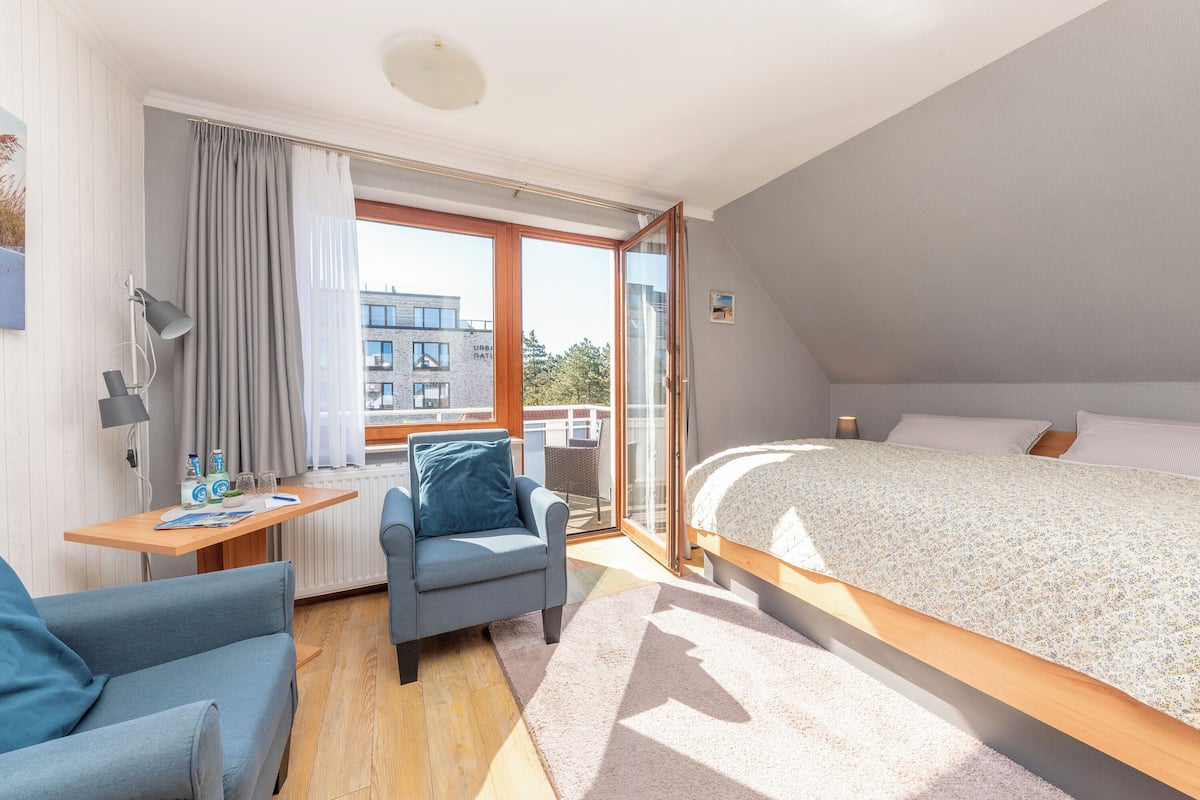 Une chambre moderne avec un grand lit, un bureau avec une chaise et une vue sur l’extérieur.