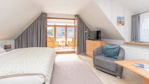 Un dormitorio con cama, sofá, televisión, escritorio y balcón.