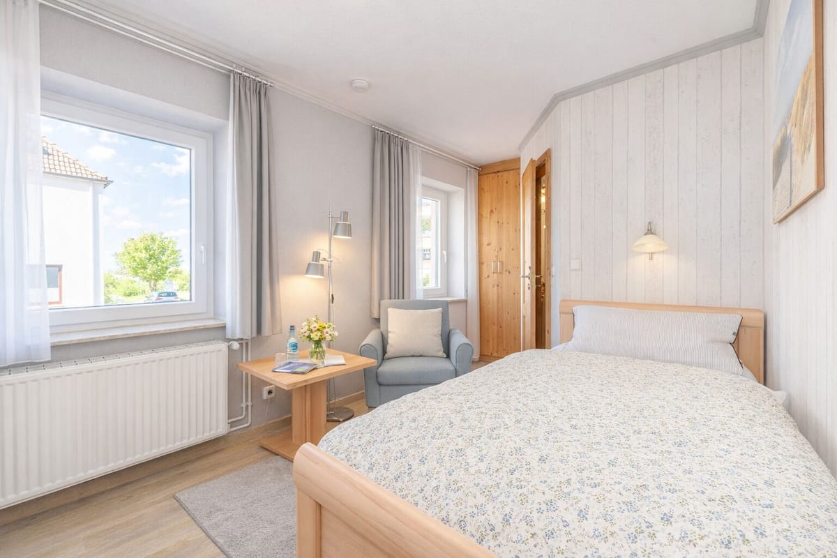 Une chambre à coucher avec un grand lit, une table de chevet avec une lampe, une chaise et une fenêtre avec des rideaux.