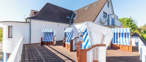 A deck with lounge chairs and a white building with a brown roof.
