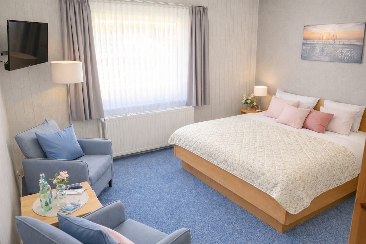 Une chambre d’hôtel comprenant un lit, un canapé, un bureau avec une lampe et un téléviseur fixé au mur.