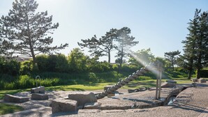 Un sitio histórico con ruinas de piedra, una fuente y un camino pavimentado rodeado de árboles.