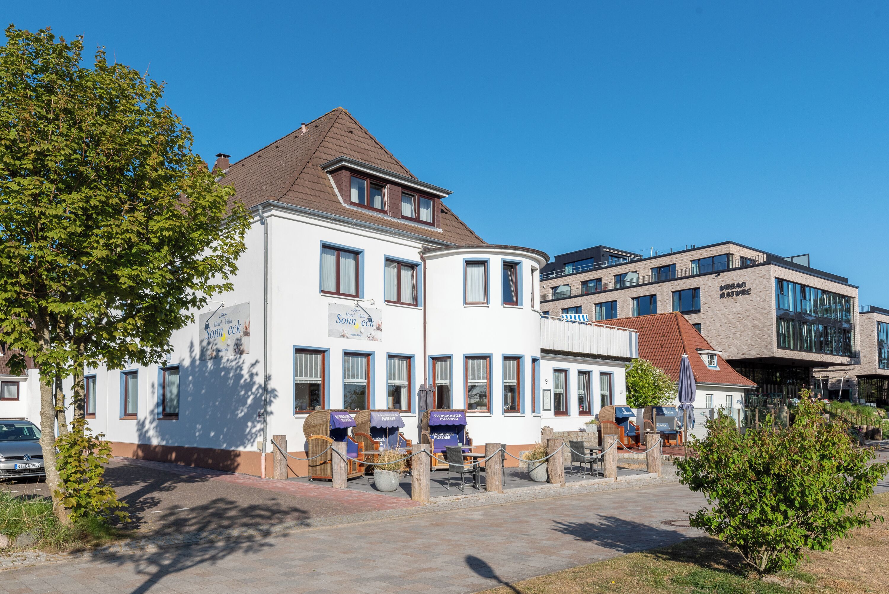 Ein zweistöckiges Gebäude mit weißer Fassade, zahlreichen Fenstern und einer abgerundeten Hausecke.
