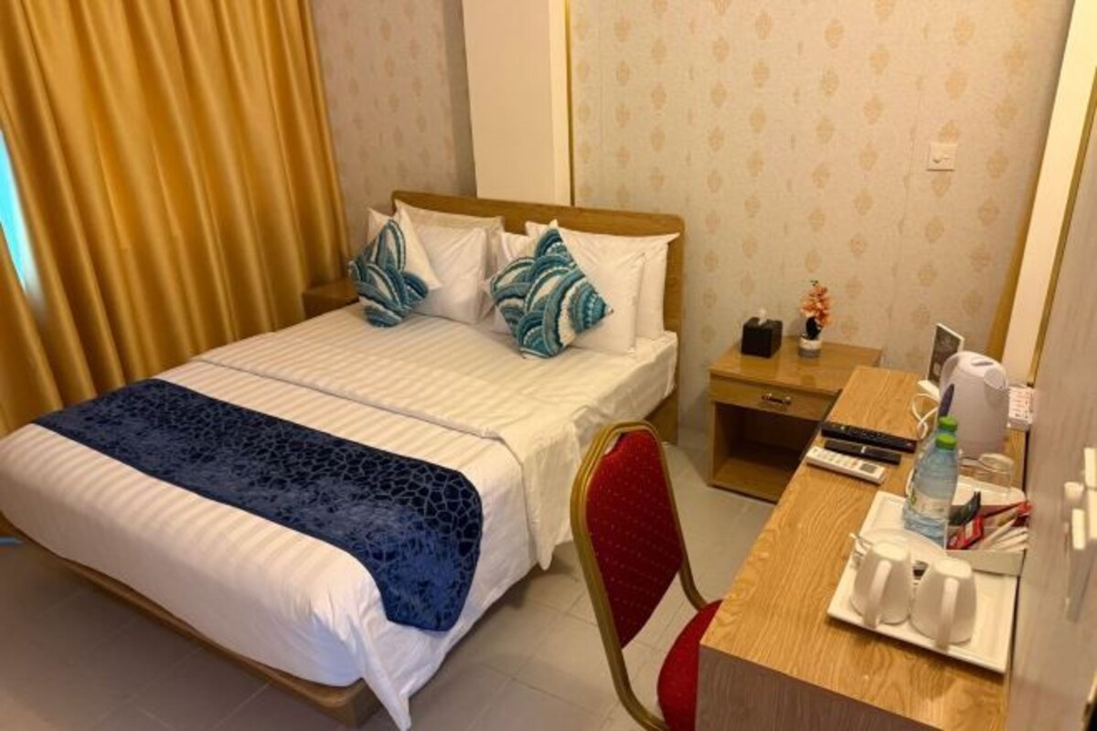 A hotel room with a bed, a desk, a chair, and a nightstand.