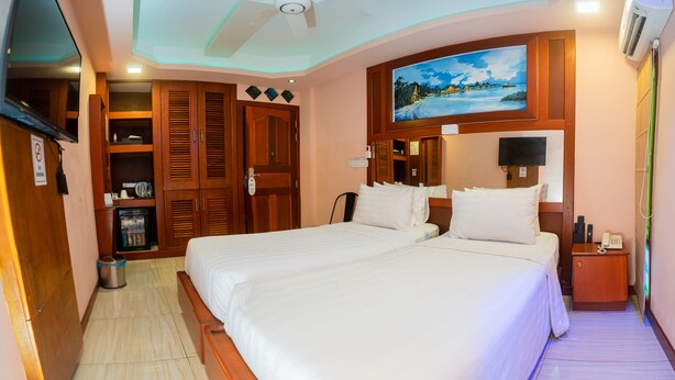 A hotel room with two beds, wooden wardrobe, a painting, and a ceiling fan. - ZAN LODGE (Malé)
