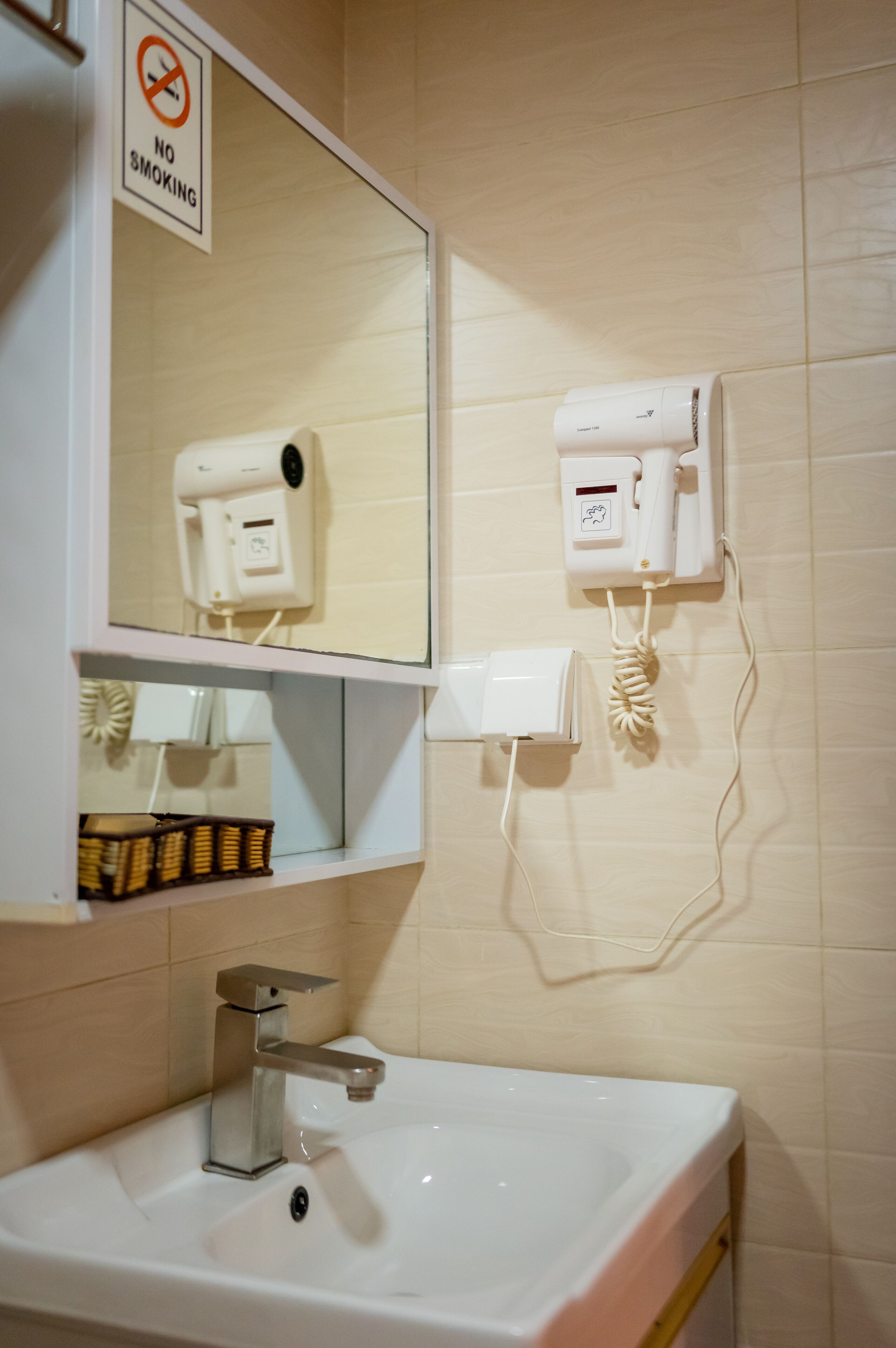 A bathroom with a sink, a mirror, a hairdryer, and a no-smoking sign.