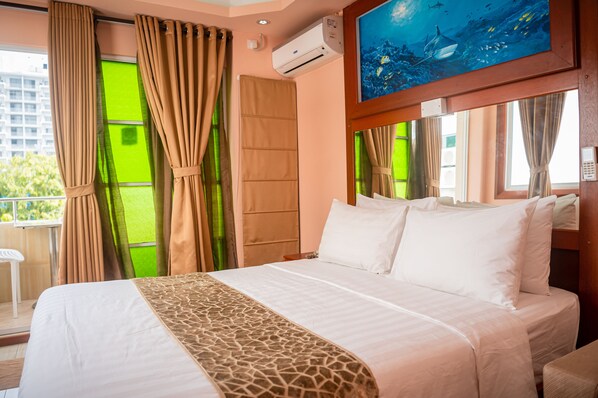 A hotel room with a bed, curtains, a painting, and a view of the city. - ZAN LODGE (Malé)
