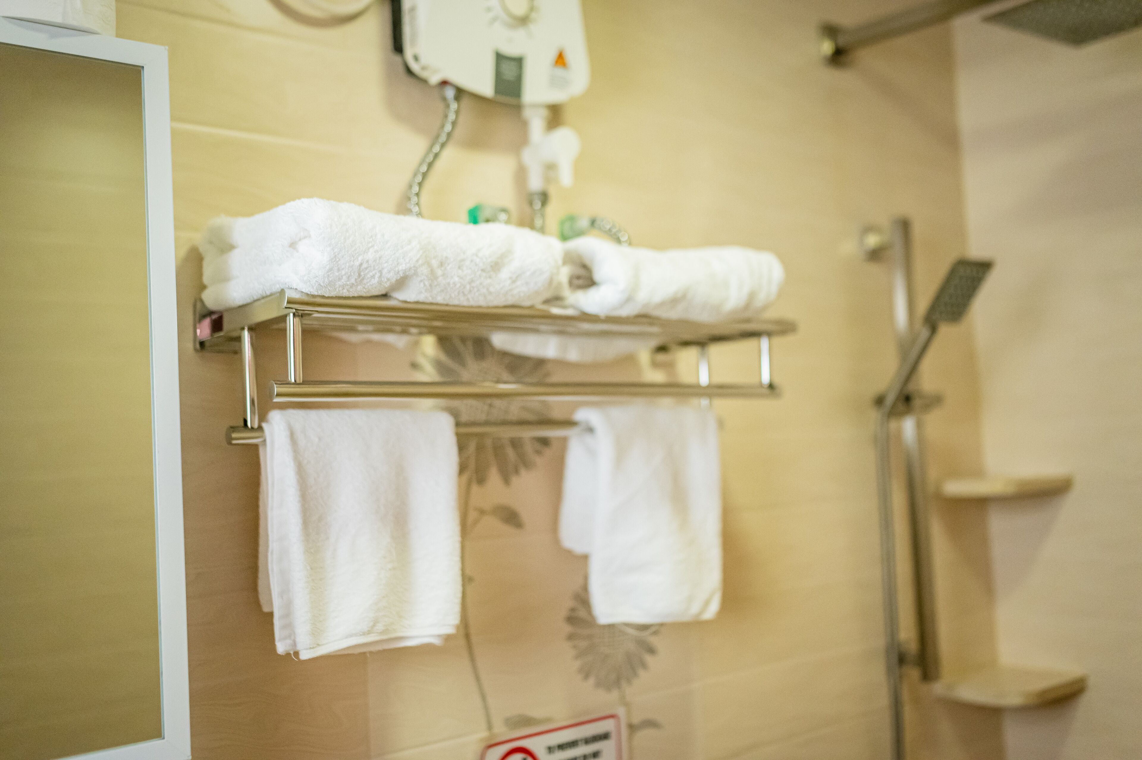 A bathroom with a towel rack holding several white towels, a showerhead, and a sign on the wall.