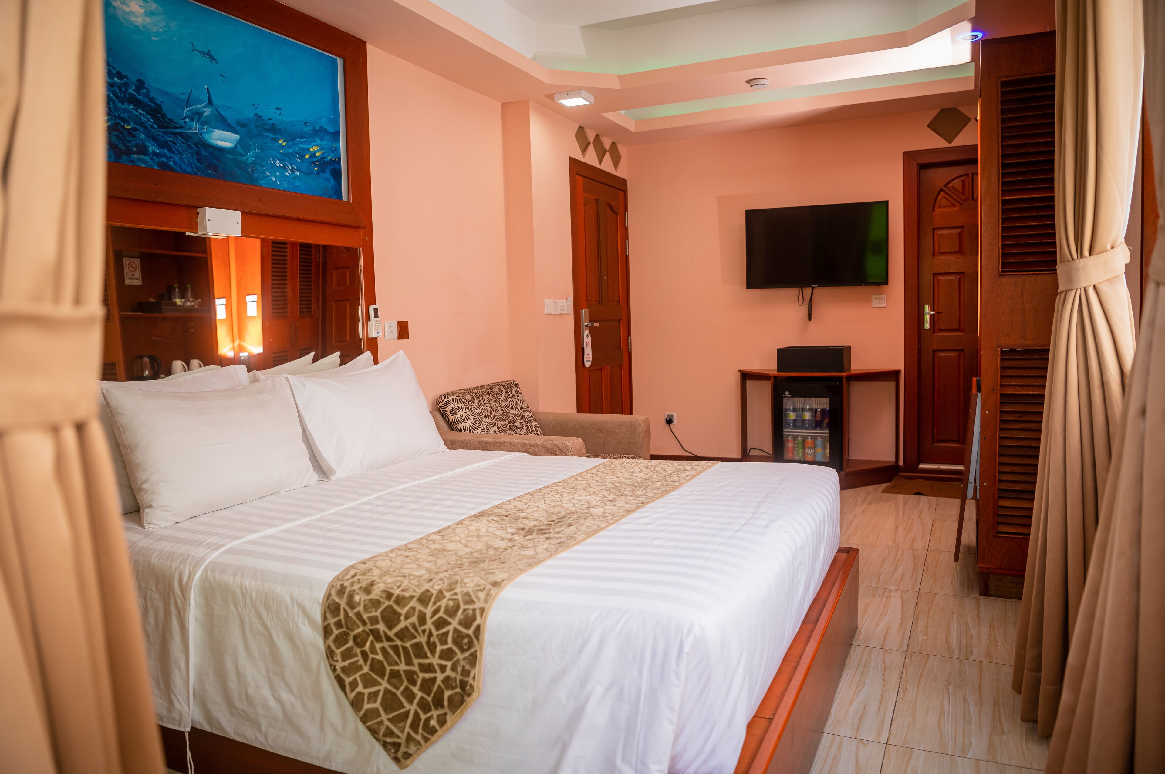 Una habitación de hotel con una cama grande, un televisor montado en la pared y un cuadro sobre la cama.