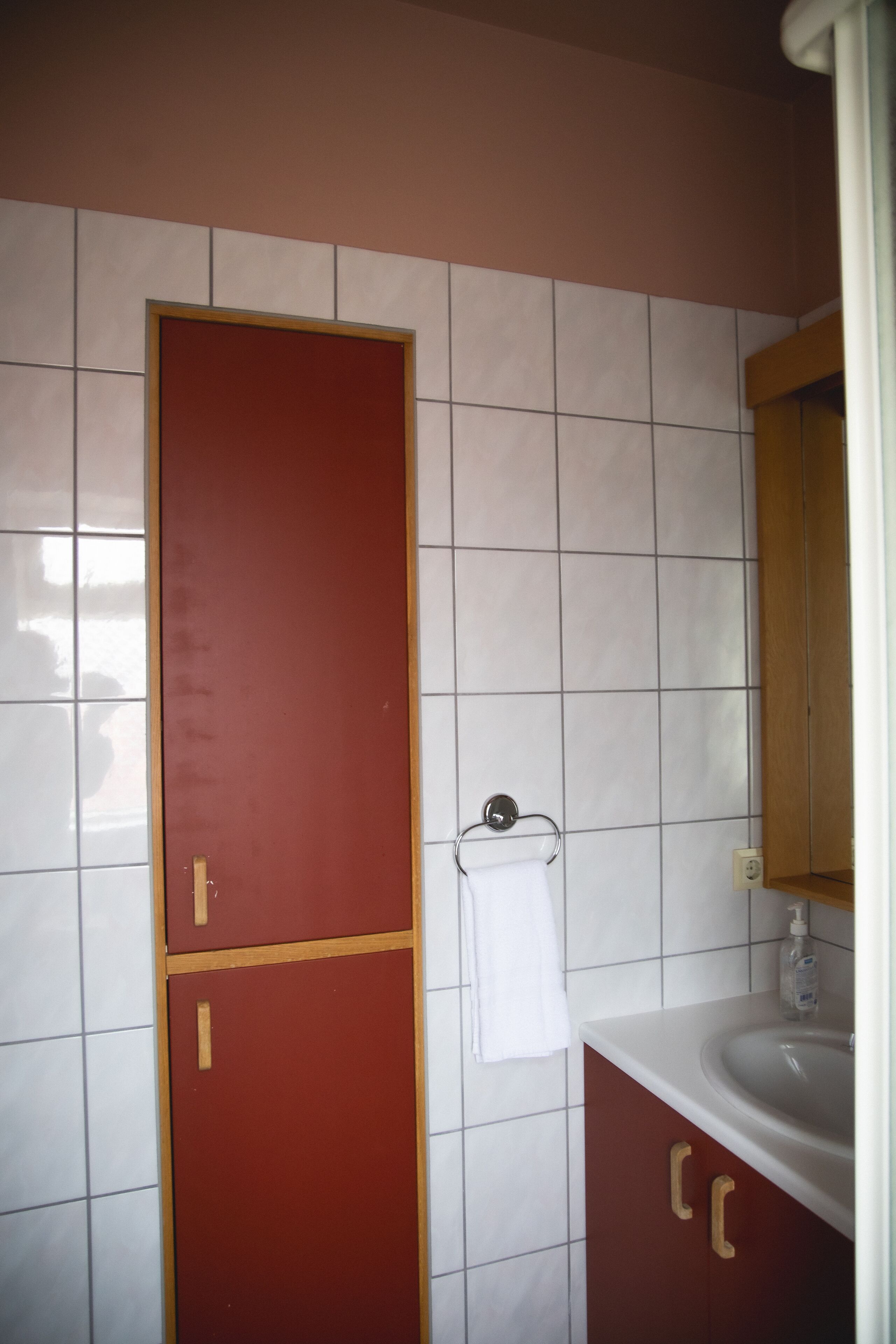 A bathroom with a red door, white tiled walls, a white sink, and a mirror.