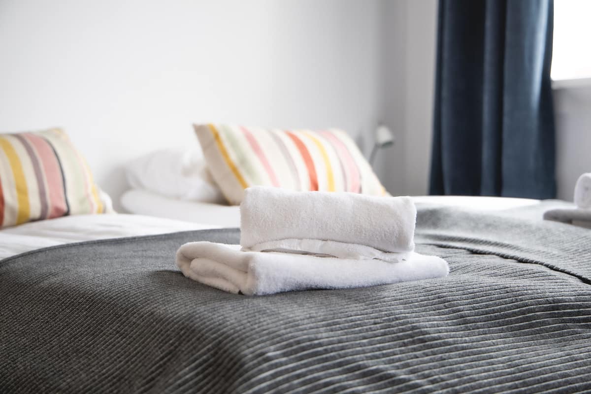 Cama bem arrumada com toalha branca dobrada e almofadas listradas.
