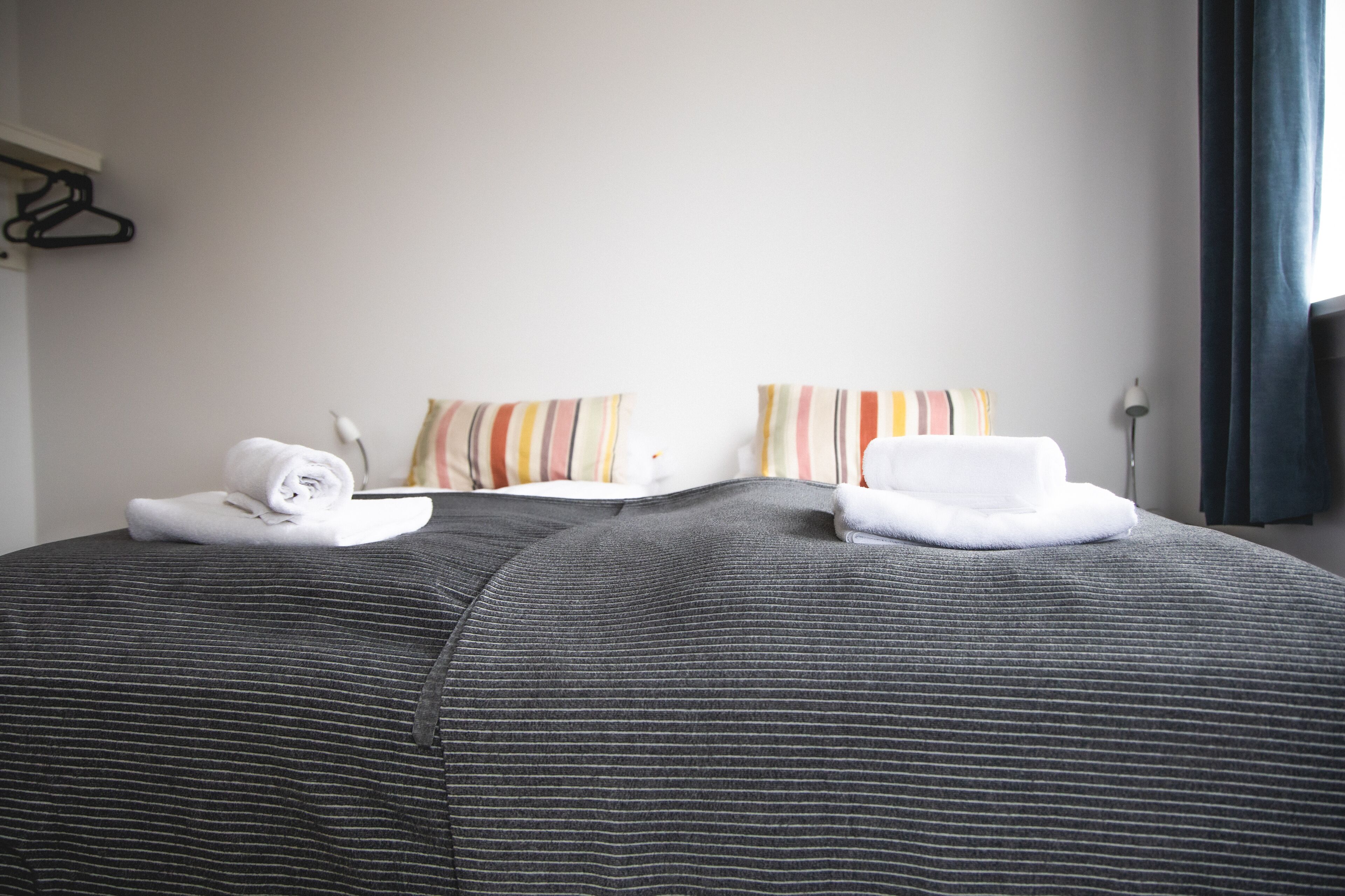 A neatly made bed with striped bedding and two pillows, a folded towel, and a bedside lamp.