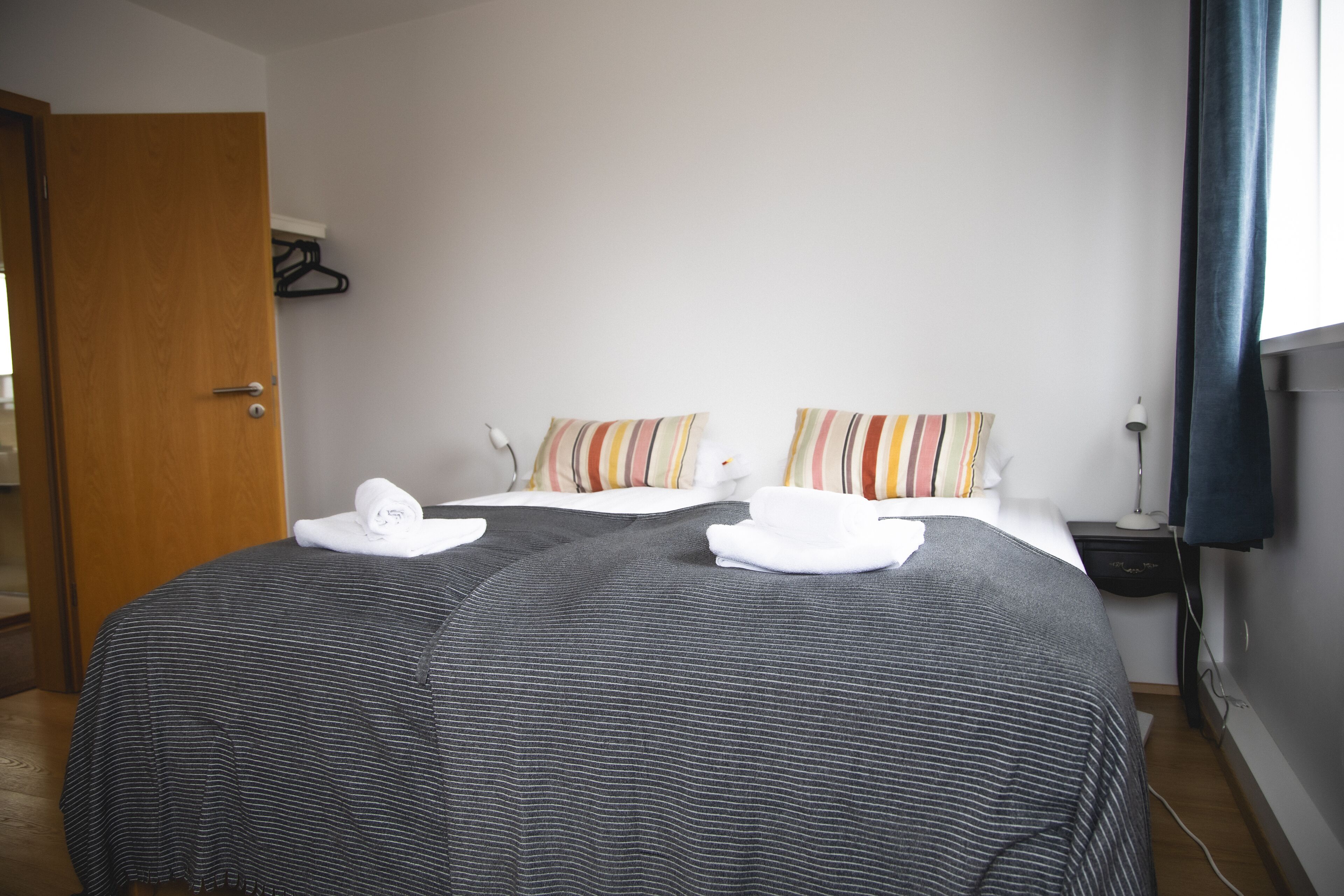 A hotel room with a bed, two pillows, a nightstand, a lamp, and a window with curtains.