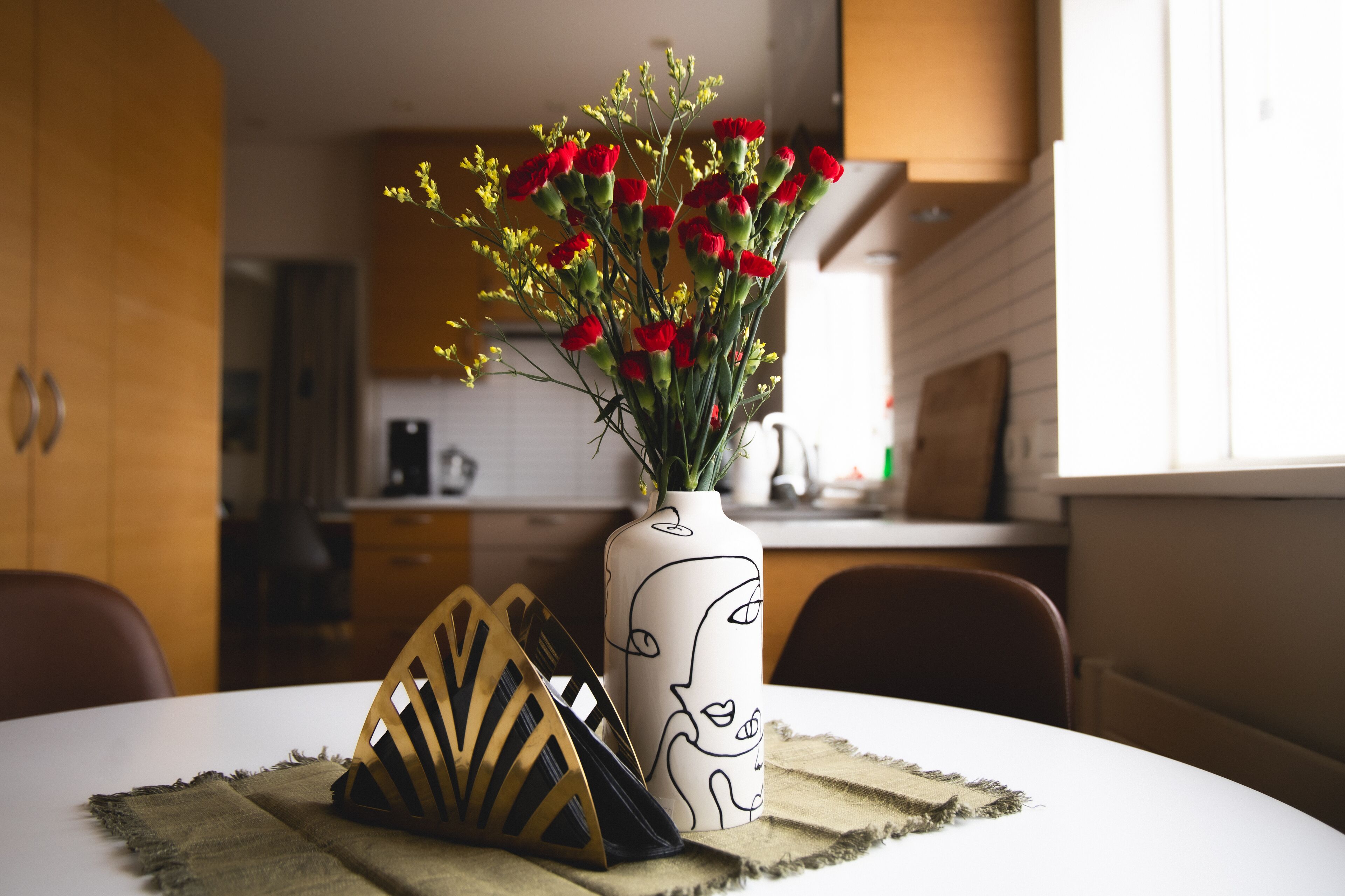 Ein Esstisch mit einer Vase roter Blumen, einem dekorativen Holzobjekt und einer Tischläufer.
