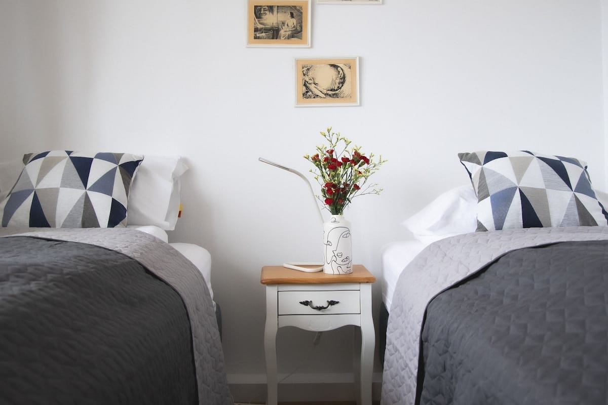 Quarto com duas camas, uma mesa de cabeceira e uma parede com três quadros.