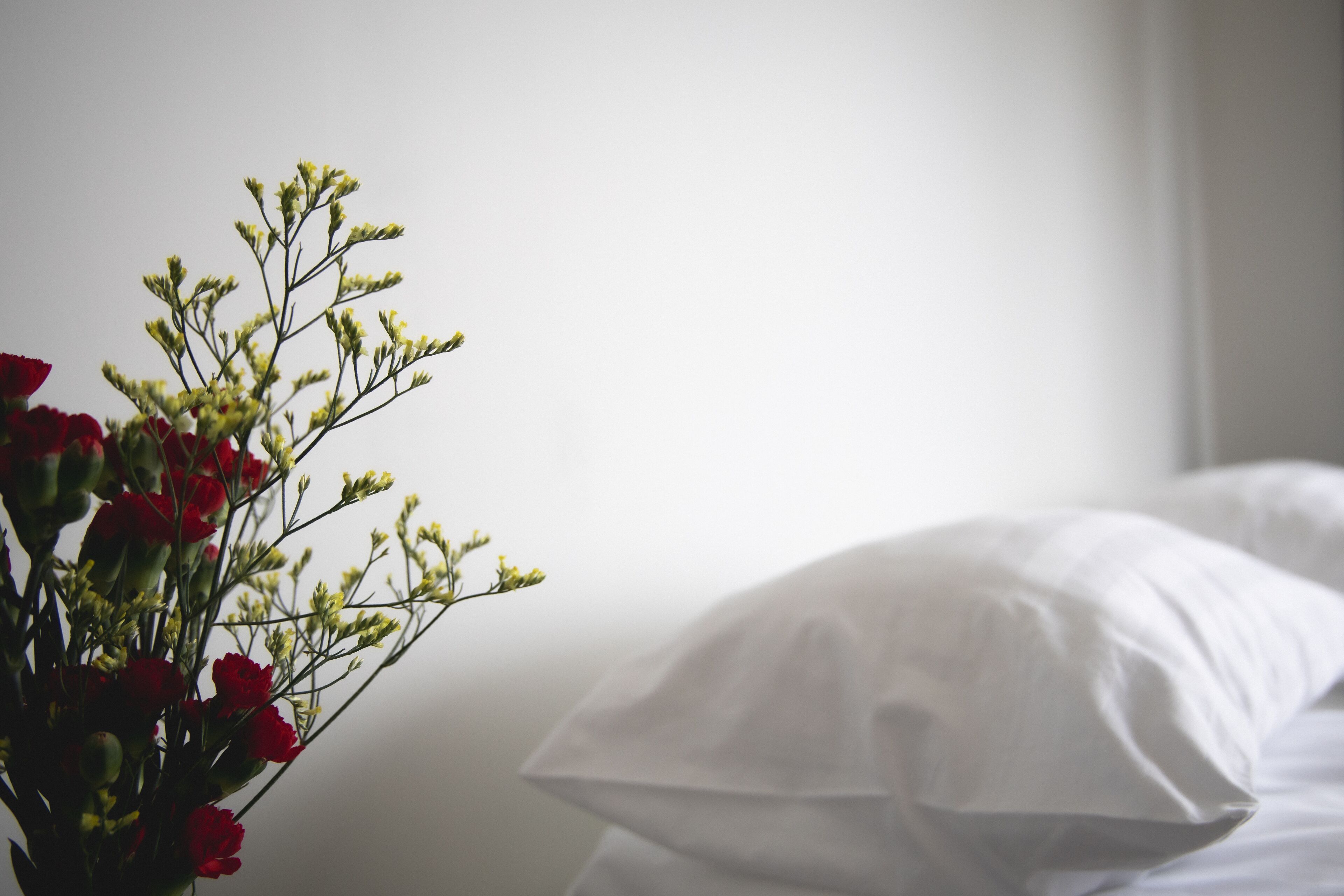 Una cama con sábanas blancas y un ramo de flores rojas y amarillas en un florero.