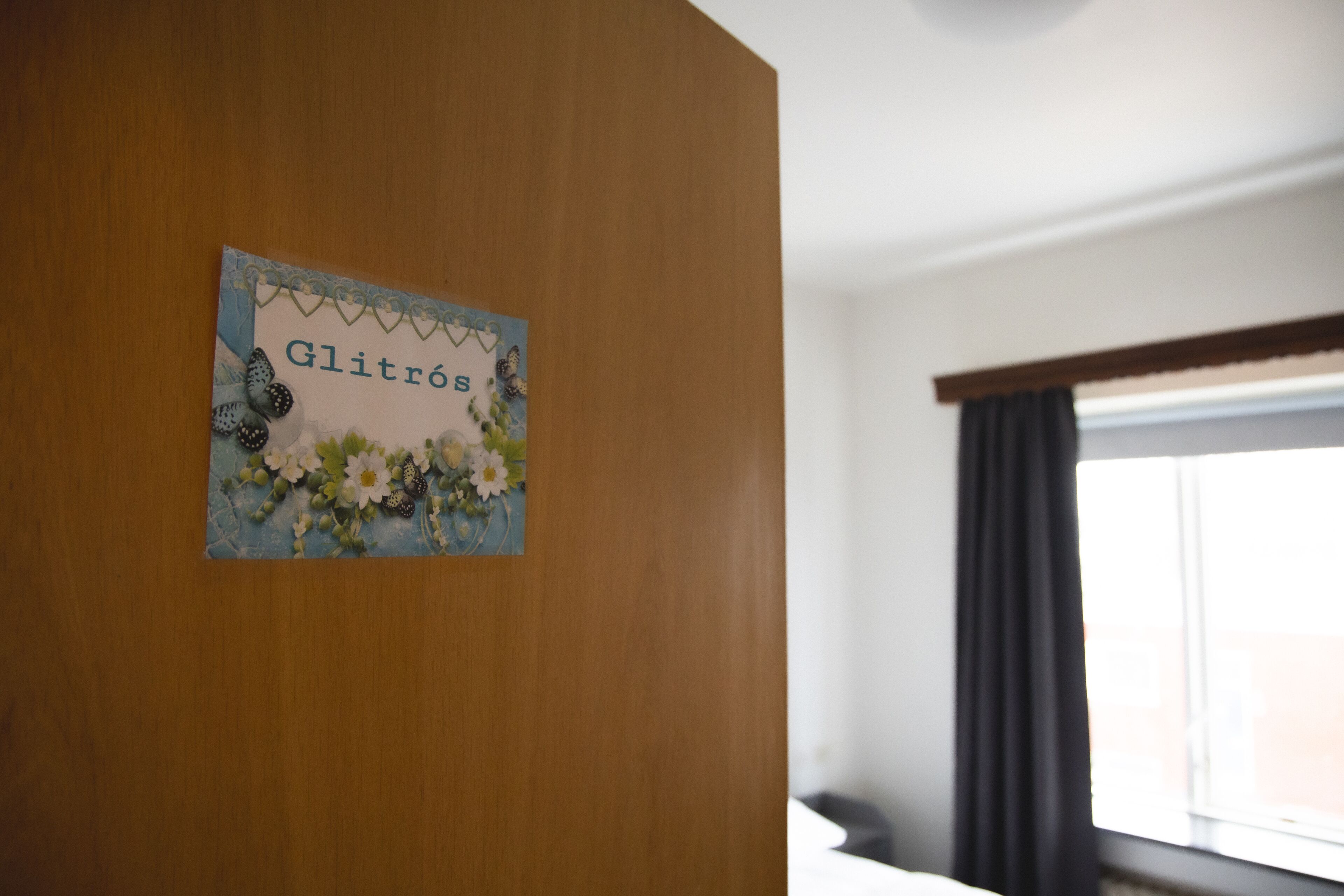 A wooden wall with a sign that reads "Glitros" and a window with curtains.
