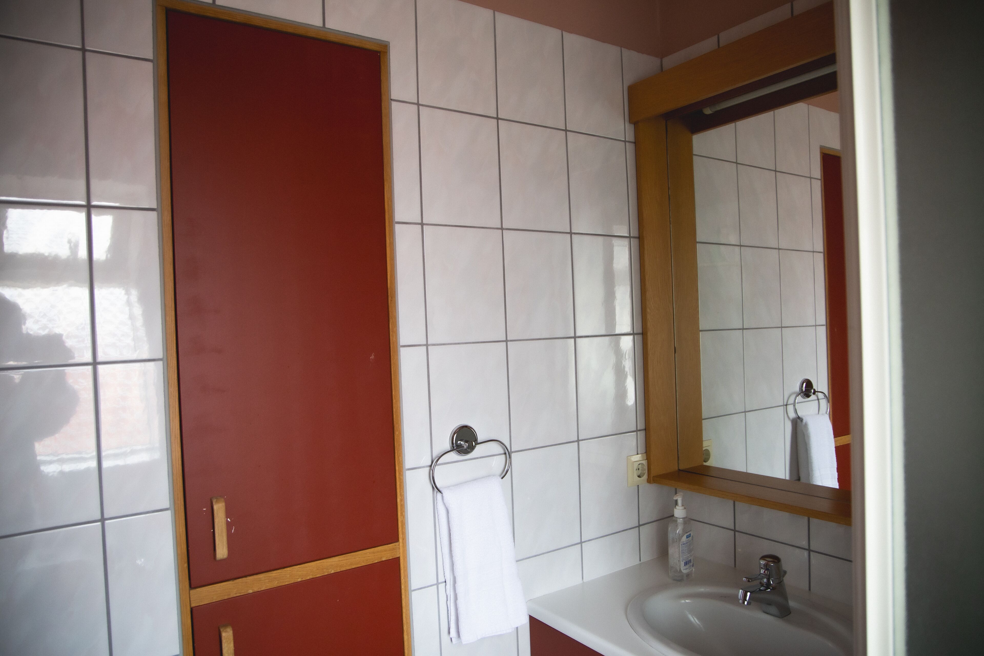 A bathroom with a white sink, a mirror, and a red door.