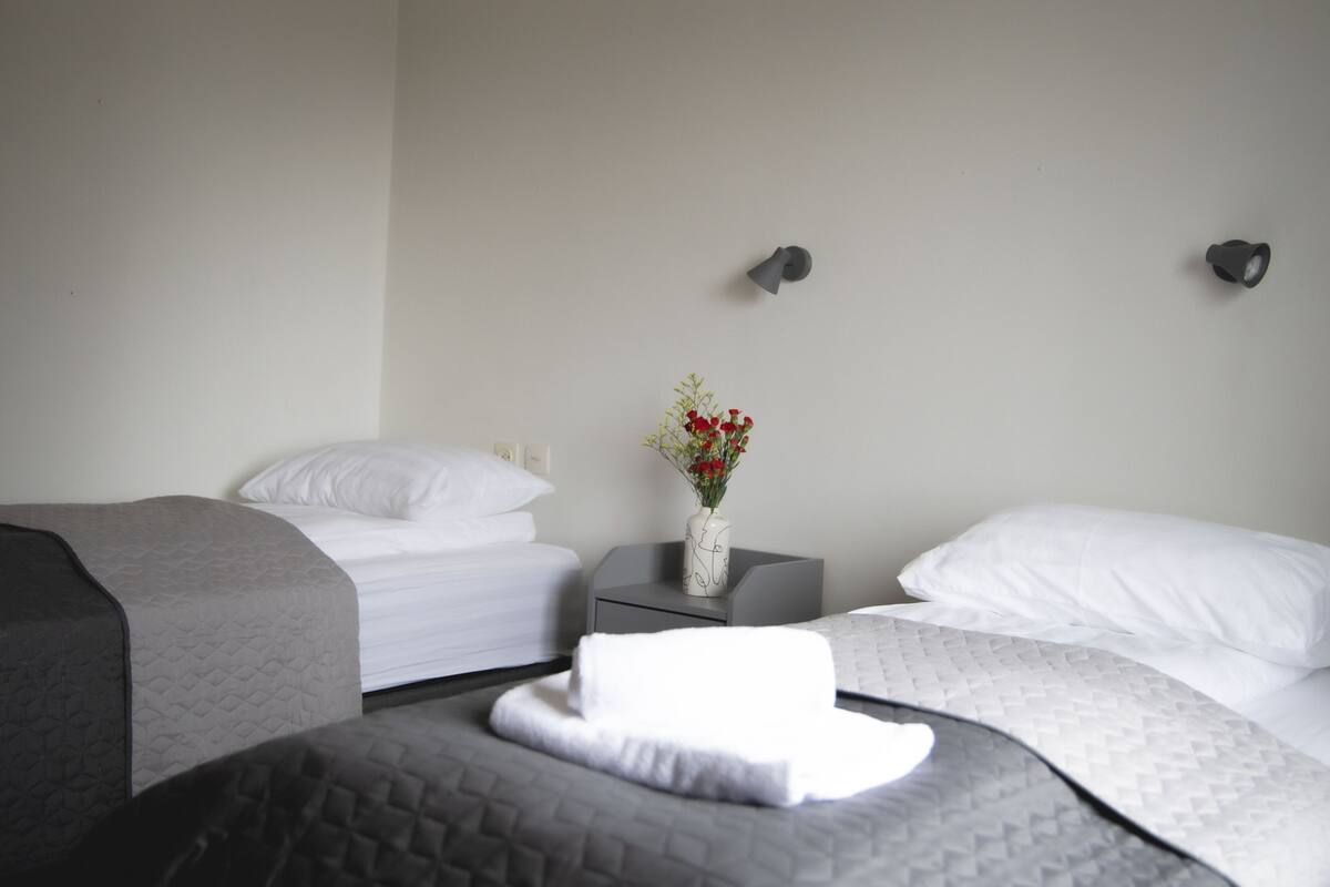 Quarto de hotel com duas camas, uma mesa de cabeceira com um vaso de flores e uma luminária na parede.
