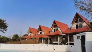 A hotel with multiple buildings, a swimming pool, and a white wall in the foreground. - Hotel Sonajhurir Adda - Shantiniketan  (Bolpur)
