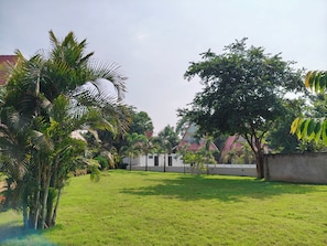A grassy outdoor area with trees and a building with a red roof. - Hotel Sonajhurir Adda - Shantiniketan (Bolpur)