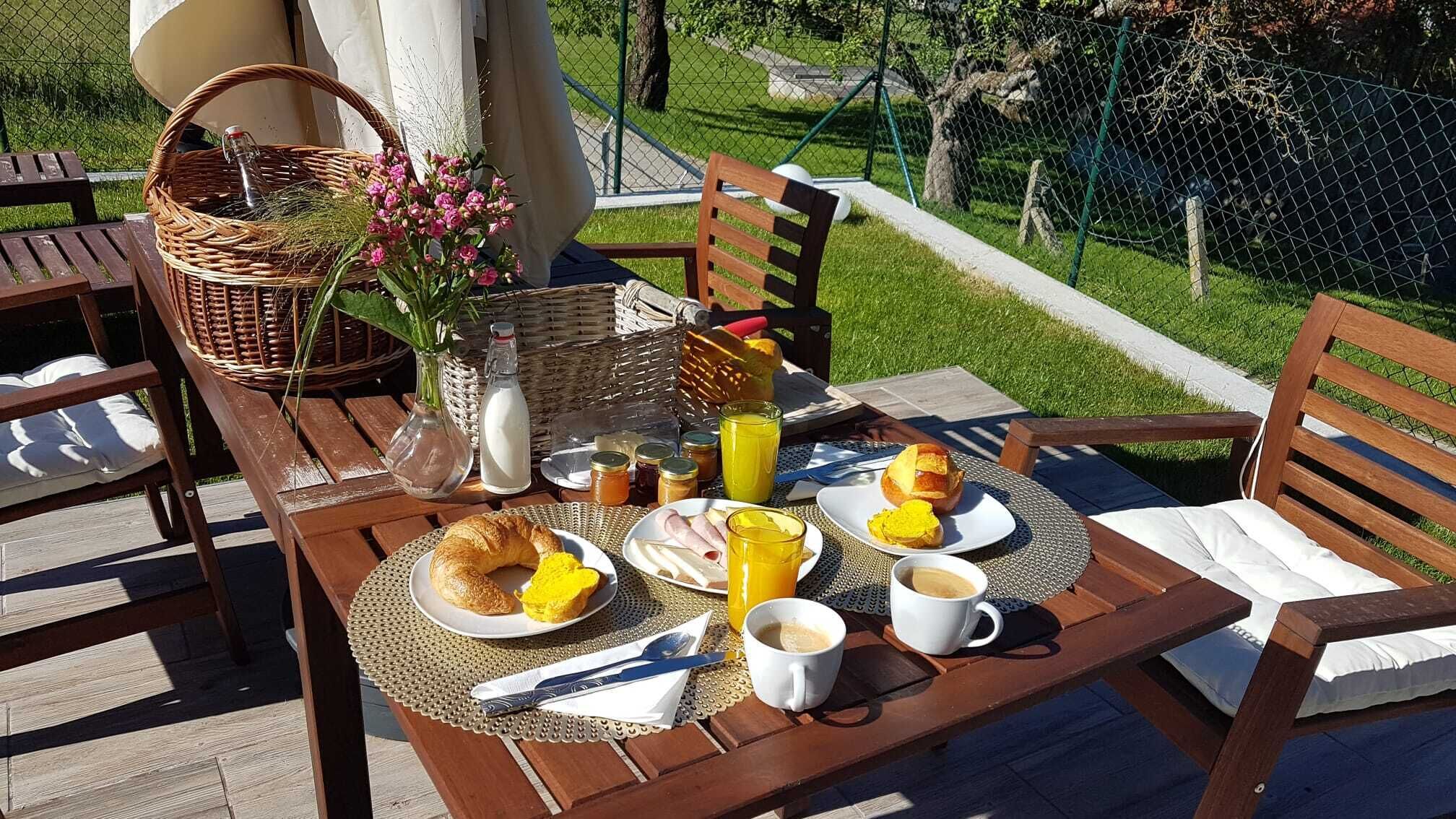 A breakfast table set outdoors with croissants, eggs, juice, and coffee.