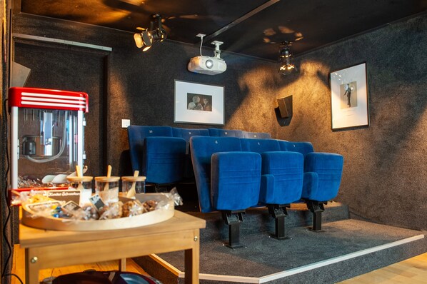 A cinema room with blue seating, a popcorn machine, and a projector on the ceiling. - Cinéma Enchanté - cinéma & bain nordique (Siviriez)