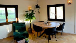 Un coin repas avec une table ronde en bois, des chaises noires, un canapé vert et une plante suspendue.