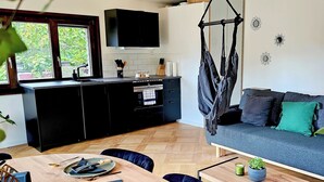 Une cuisine moderne avec des meubles de couleur noire, une table à manger en bois et un fauteuil suspendu.