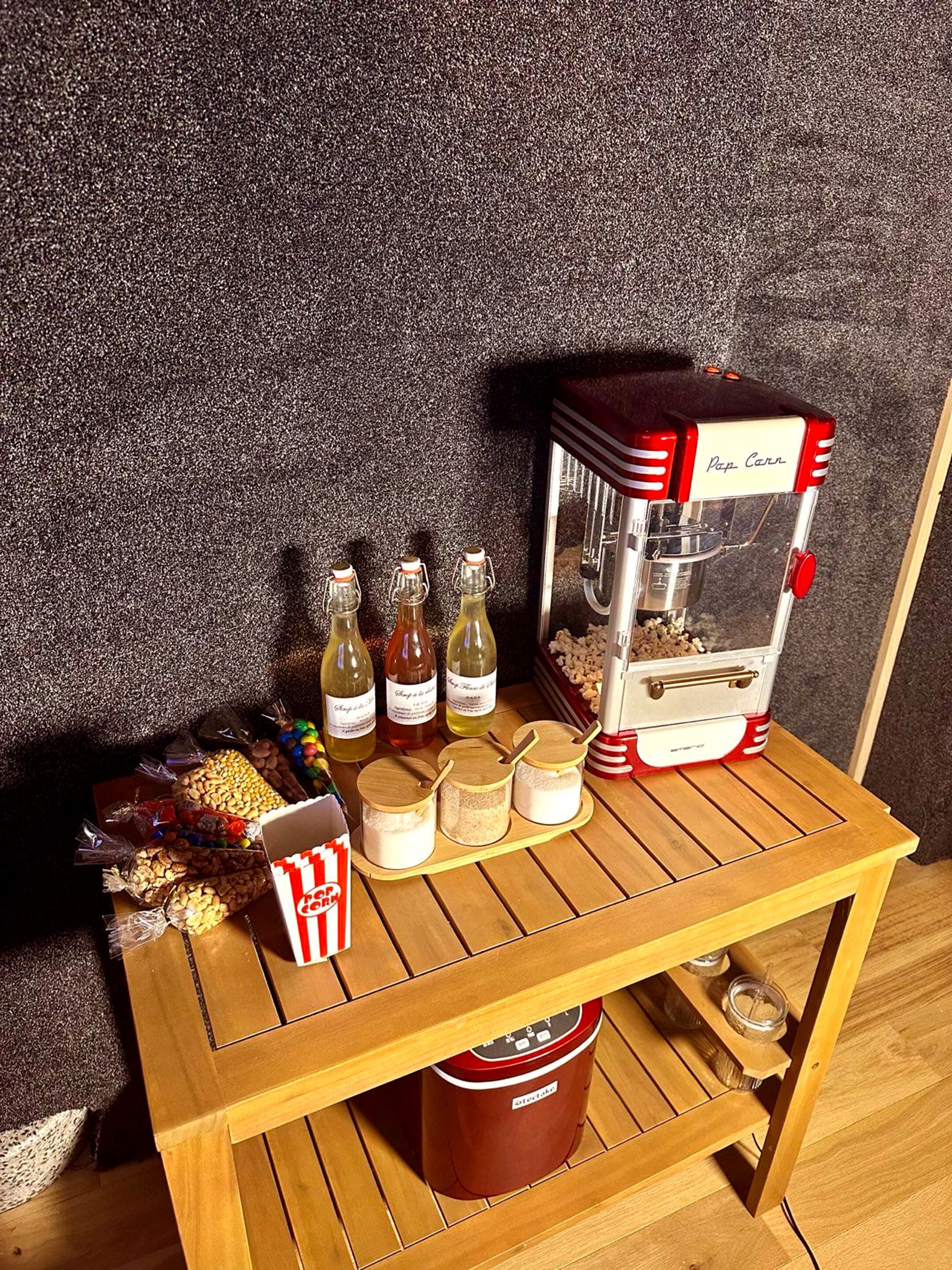 Una macchina per popcorn con bottiglie d'olio e chicchi di mais su un tavolo di legno.