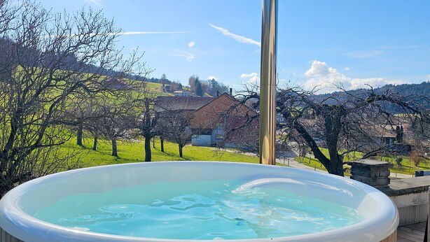 Un bain à remous sur une terrasse en bois, offrant une vue panoramique sur les maisons et les arbres en arrière-plan.