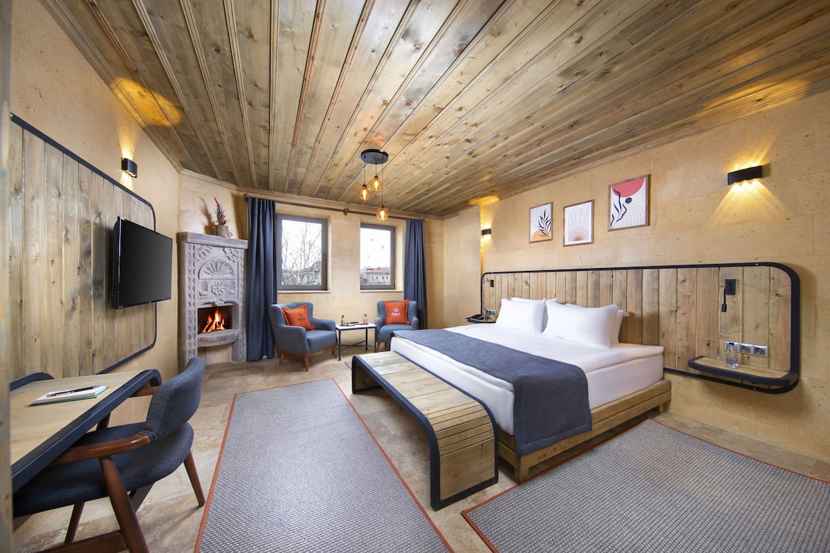 A wooden-paneled room with a bed, a desk, chairs, a fireplace, and artwork on the walls.
