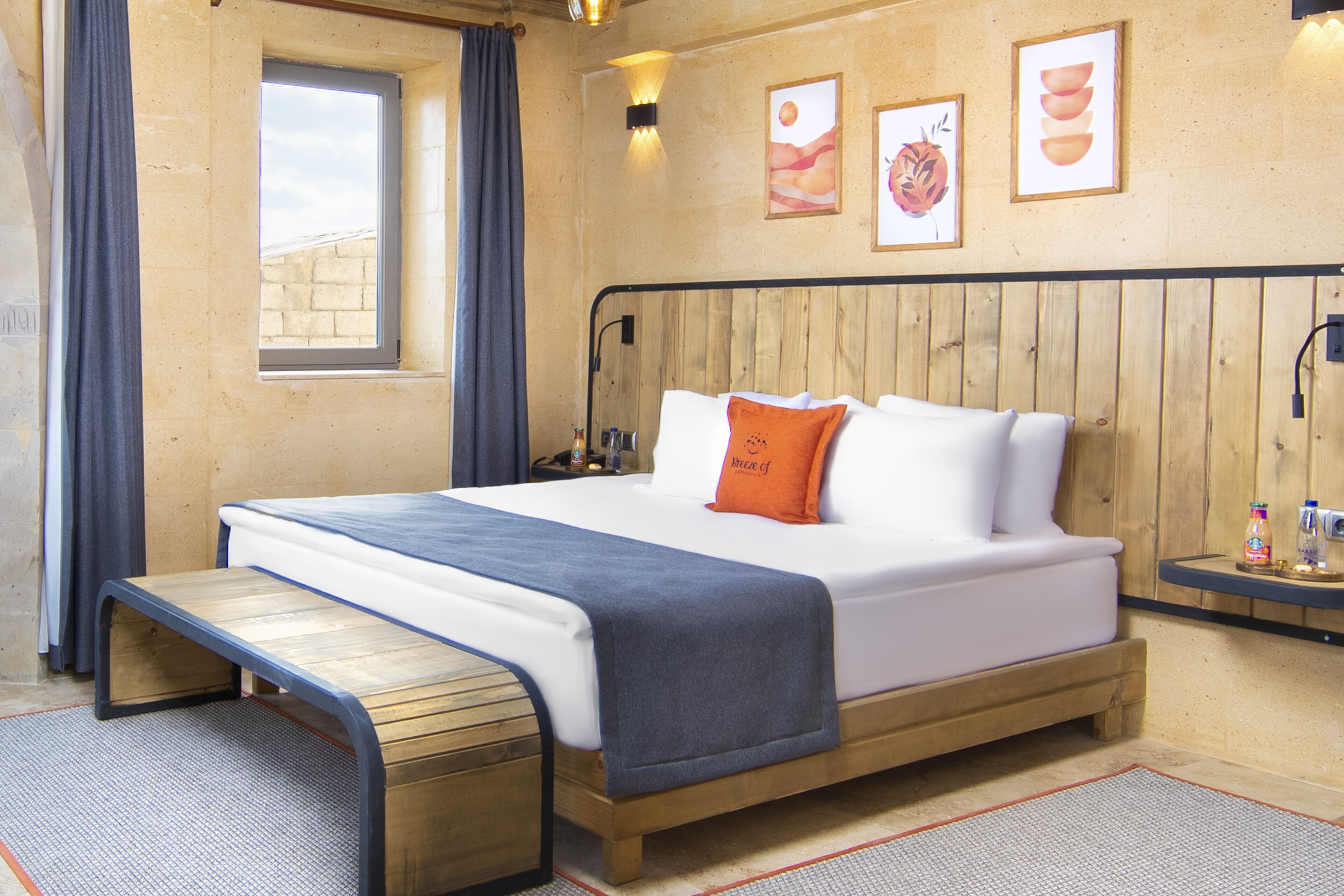 A hotel room with a wooden bed, a small desk, a window with curtains, and wall-mounted artwork.