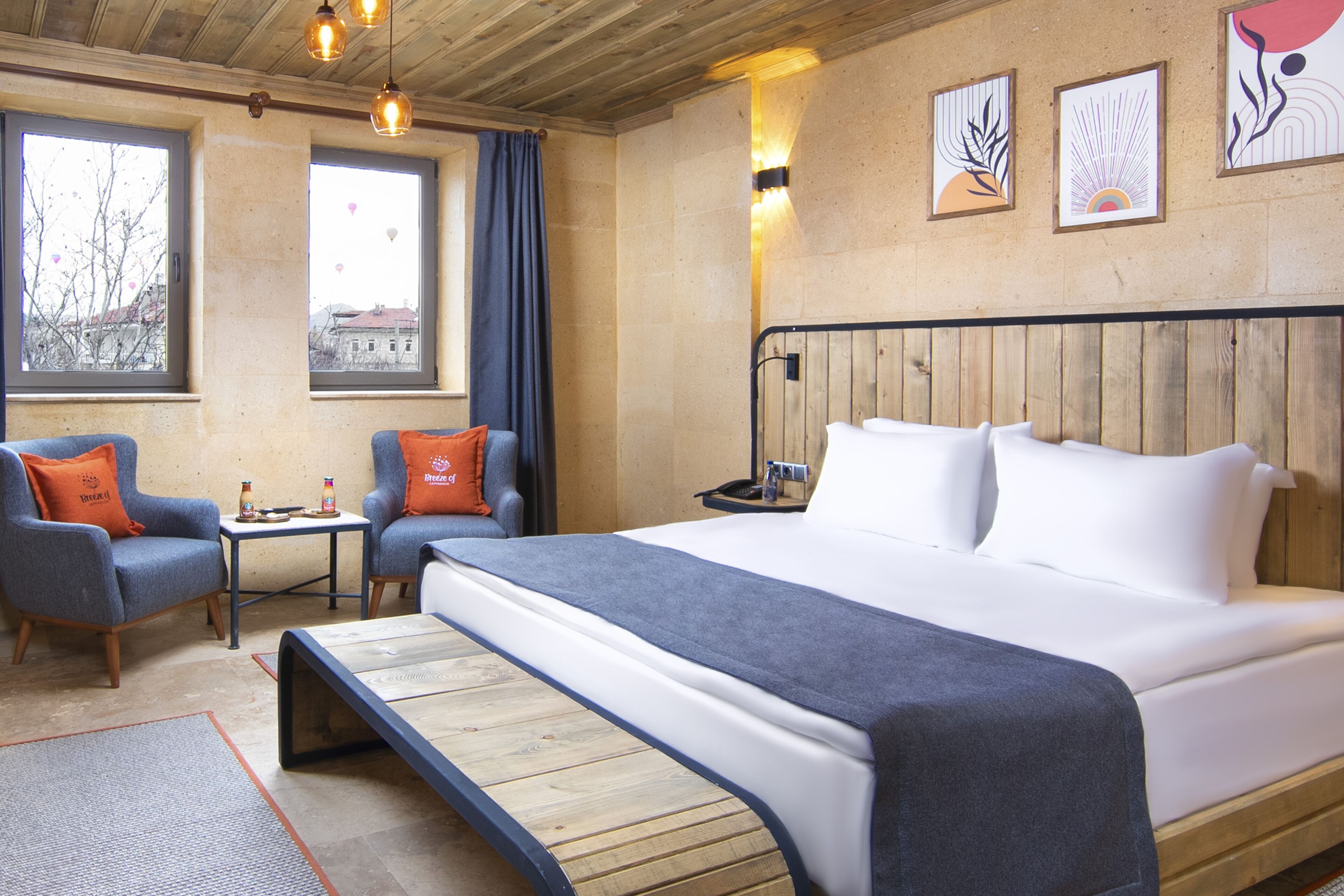 Habitación de hotel con una cama grande, dos sillones, una mesita y vistas de la ciudad a través de amplias ventanas.
