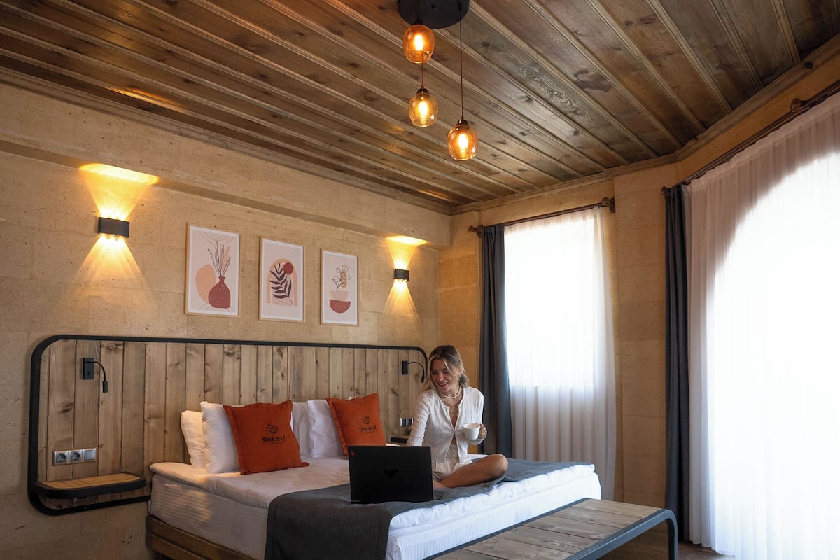 A wooden-paneled room with a bed, a laptop, and a cup on the bed.