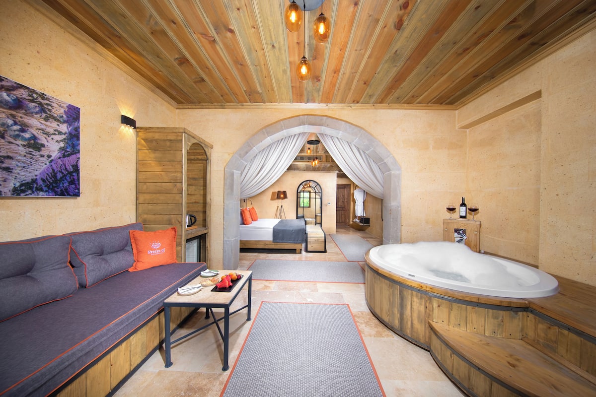 A spa room with a wooden ceiling, a large bathtub, a sofa, and a bed.