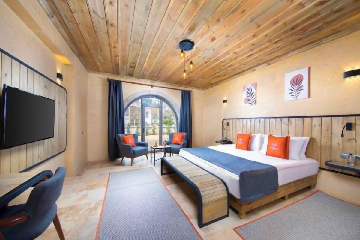A hotel room with a bed, seating area, television, and a large window.