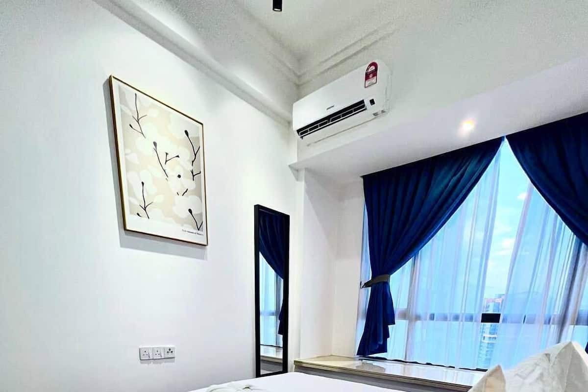 Una habitació d'hotel amb un llit gran, aire condicionat al sostre, una finestra amb cortines blaves i una obra d'art emmarcada a la paret.
