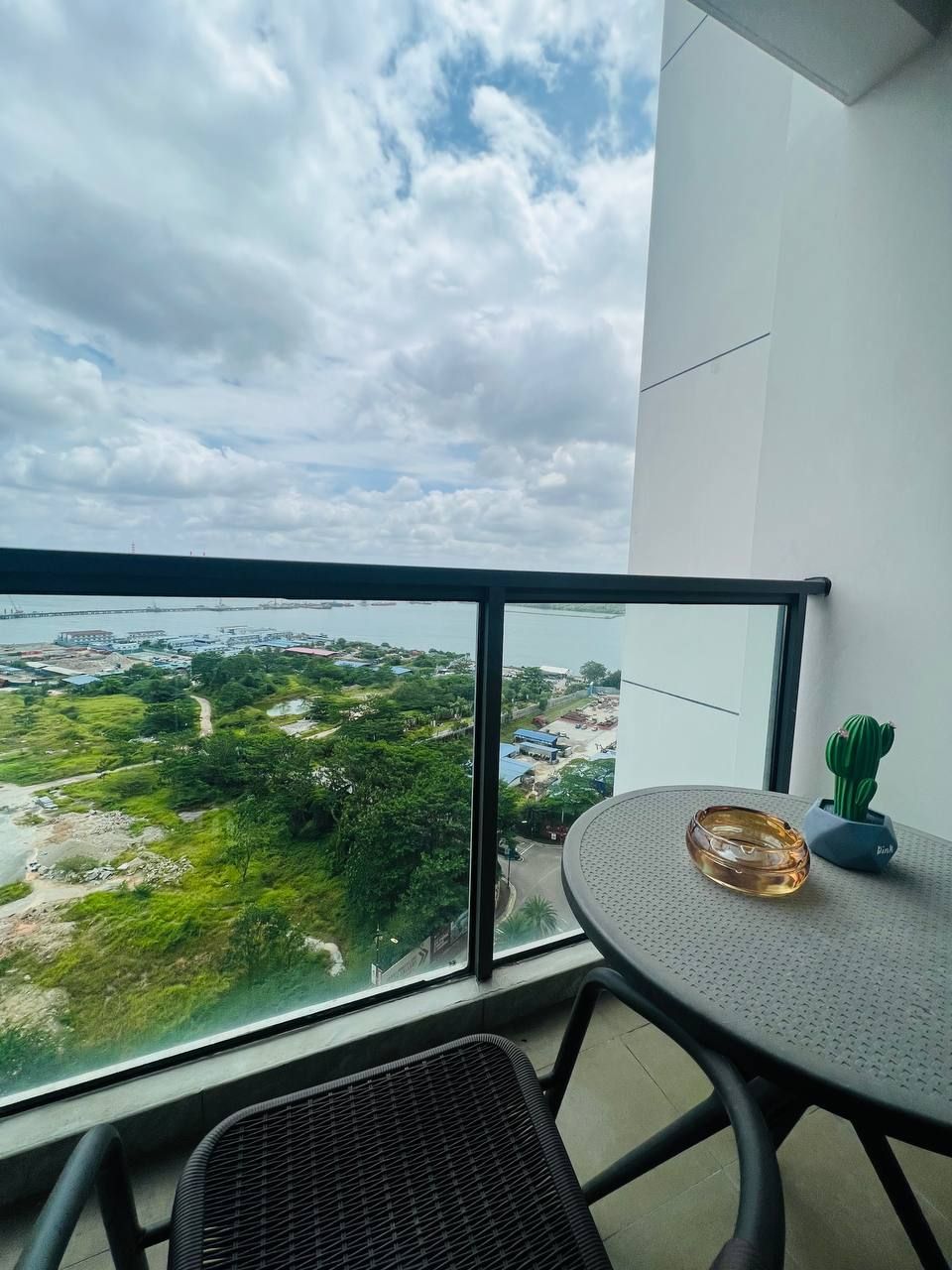 A balcony with a view of a coastal area, a round table with a glass object, and a chair.