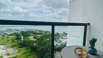 A balcony with a view of a coastal area, a round table with a glass object, and a chair.