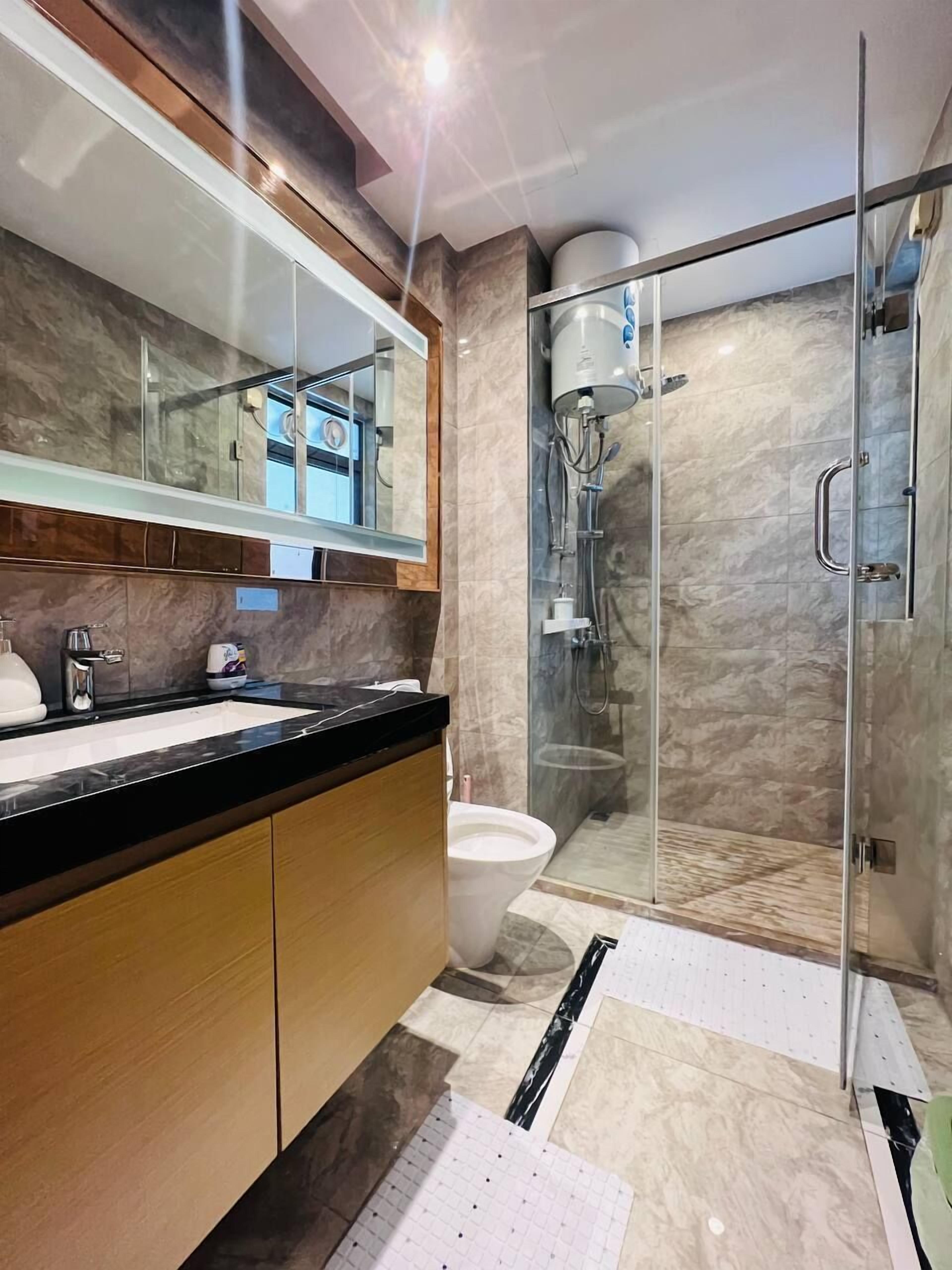 A modern bathroom with a glass shower enclosure, a large mirror, and a marble-tiled floor.