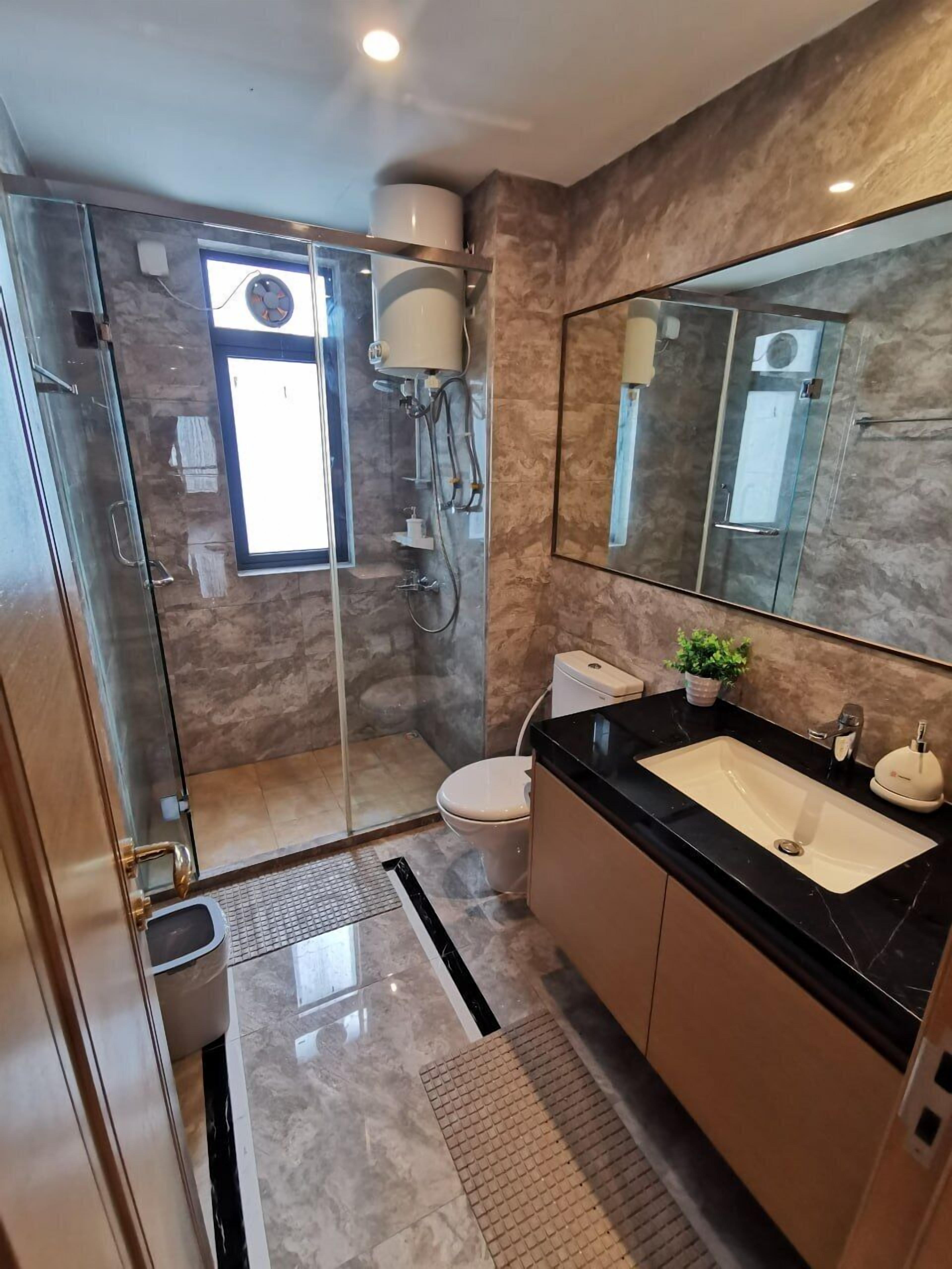 Un baño moderno con ducha de vidrio, inodoro, lavamanos con encimera negra y un espejo grande.