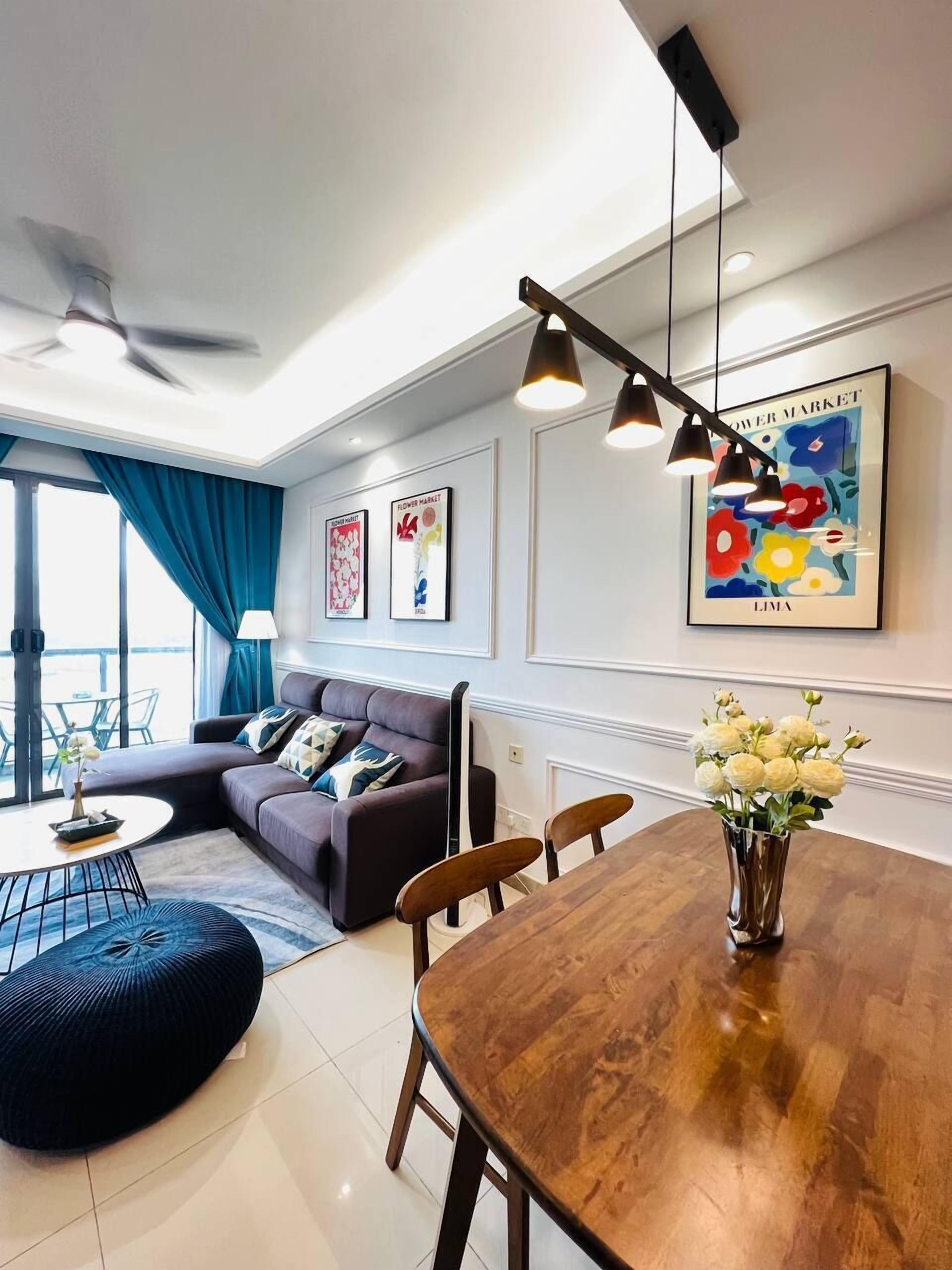 A modern living room with a sectional sofa, a round coffee table, and a dining table with chairs. There are ceiling fans, pendant lights, and artwork on the walls.
